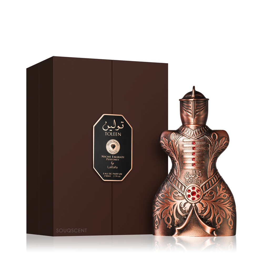 Copper-colored perfume bottle with intricate designs next to its packaging on a white background